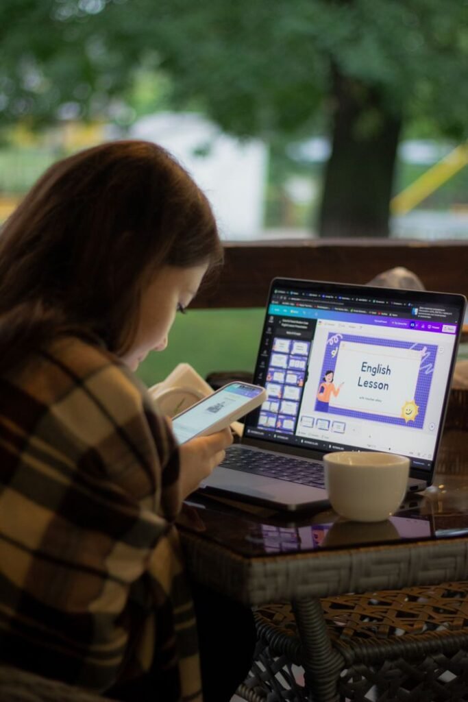 Woman using laptop for online English lesson while checking her phone.